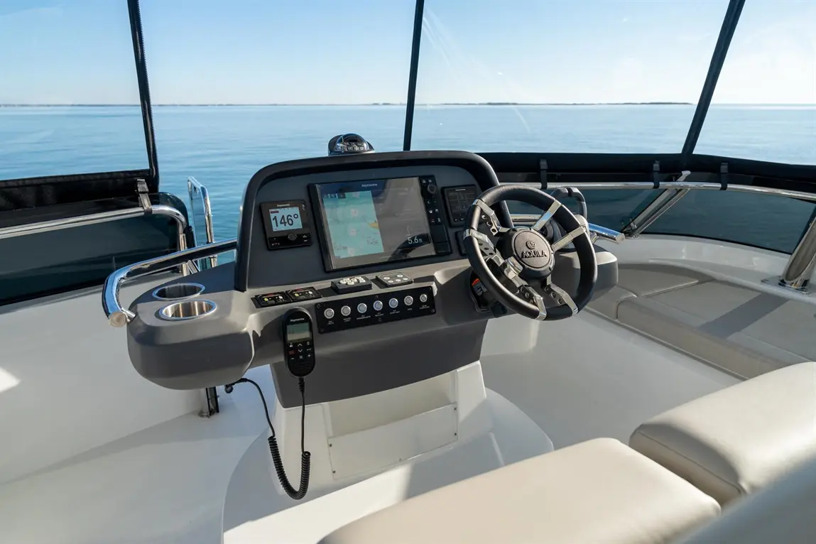 Boat cockpit showing a steering wheel, navigation screen, controls, and open water view with clear skies.